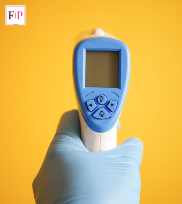 Gloved hand holding an infrared thermometer, used to check the sudden high temperature that is one of the key flu symptoms 2026