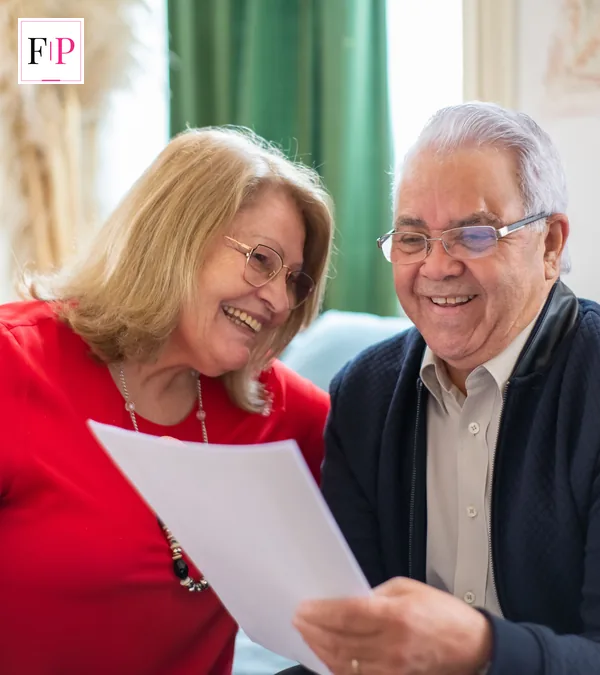 A senior couple smiling while reviewing a document together at home — checking a pension credit claim